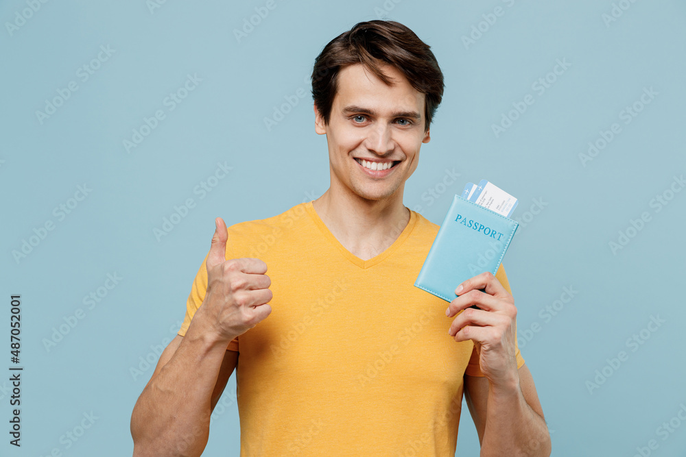 Traveler tourist man in yellow t-shirt hold passport ticket show thumb up isolated on plain pastel light blue background studio. Passenger travel abroad on weekends getaway Air flight journey concept Traveler tourist man in yellow t-shirt hold passport ticket show thumb up isolated on plain pastel light blue background studio. Passenger travel abroad on weekends getaway Air flight journey concept