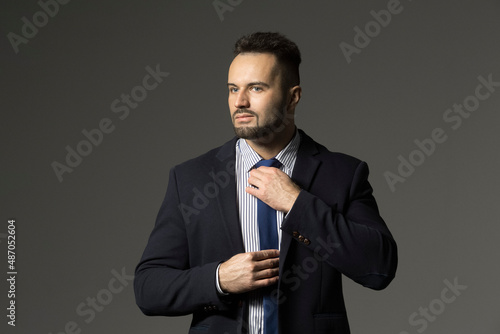 Portrait confident, stylish businessman in suit adjusting tie against black background
 photo