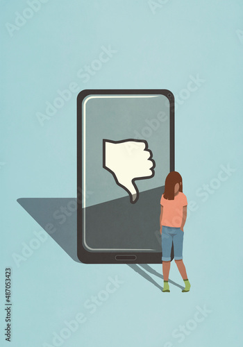 Sad girl standing next to thumbs down icon on smart phone screen
 photo