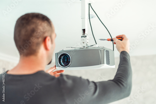 The man independently adjusts a multimedia video projector for home theater or presentations mounted on a ceiling bracket. photo