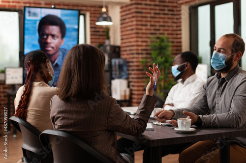 Multiethnic businesspeople with medical face mask to prevent infection with covid19 discussing company strategy with remote manager during online videocall meeting in startup office. Business call © DC Studio