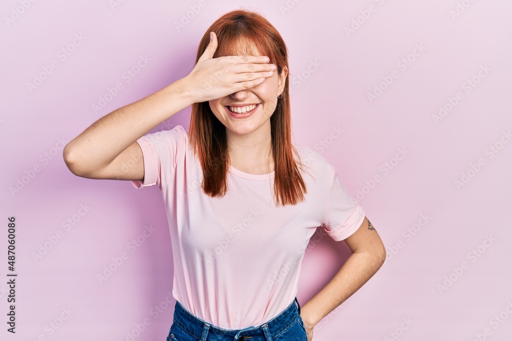 Redhead young woman wearing casual pink t shirt smiling and laughing with hand on face covering eyes for surprise. blind concept. Redhead young woman wearing casual pink t shirt smiling and laughing with hand on face covering eyes for surprise. blind concept.