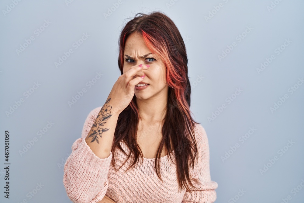 Young caucasian woman wearing pink sweater over isolated background smelling something stinky and disgusting, intolerable smell, holding breath with fingers on nose. bad smell Young caucasian woman wearing pink sweater over isolated background smelling something stinky and disgusting, intolerable smell, holding breath with fingers on nose. bad smell