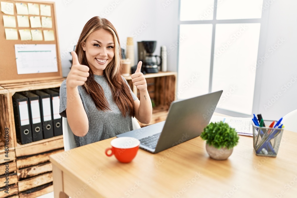 Young brunette woman working at the office with laptop success sign doing positive gesture with hand, thumbs up smiling and happy. cheerful expression and winner gesture. Young brunette woman working at the office with laptop success sign doing positive gesture with hand, thumbs up smiling and happy. cheerful expression and winner gesture.