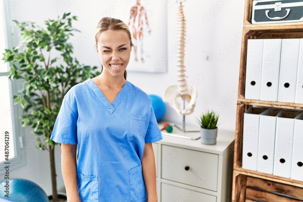 Young caucasian woman working at pain recovery clinic sticking tongue out happy with funny expression. emotion concept. Young caucasian woman working at pain recovery clinic sticking tongue out happy with funny expression. emotion concept.