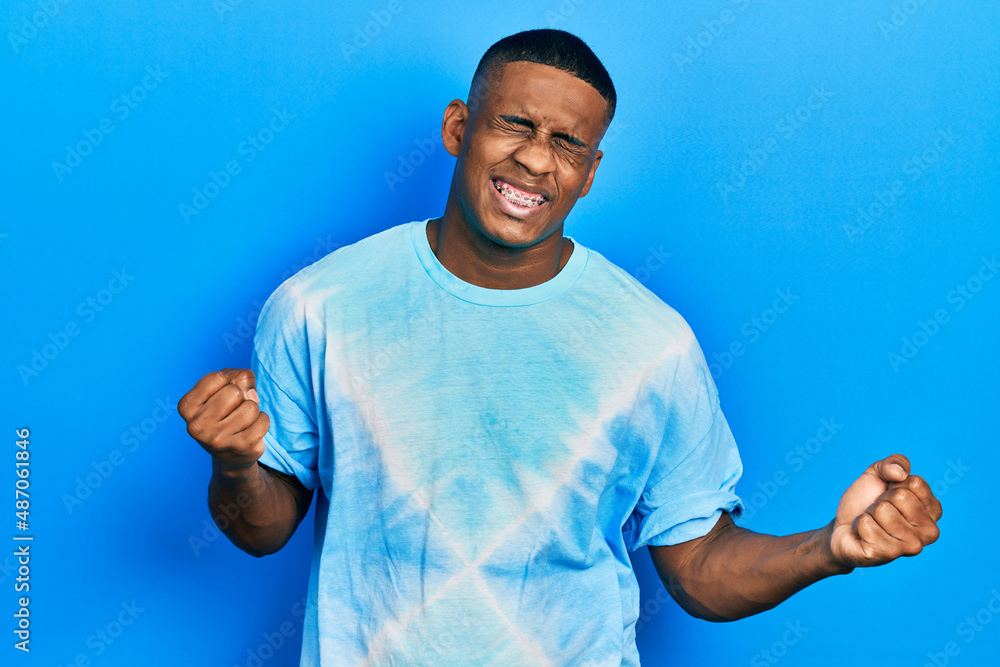 Young black man wearing tye die t shirt very happy and excited doing winner gesture with arms raised, smiling and screaming for success. celebration concept. Young black man wearing tye die t shirt very happy and excited doing winner gesture with arms raised, smiling and screaming for success. celebration concept.