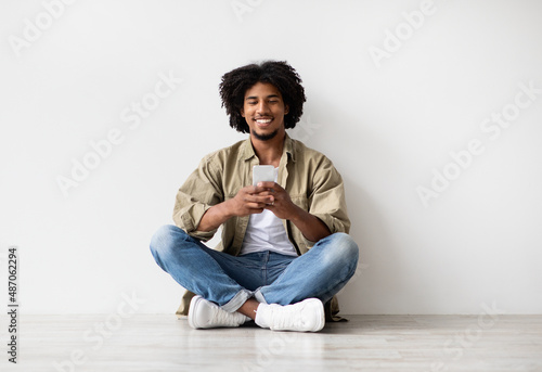 Online Communication. Happy Black Man Messaging On Smartphone While Relaxing On Floor © Prostock-studio