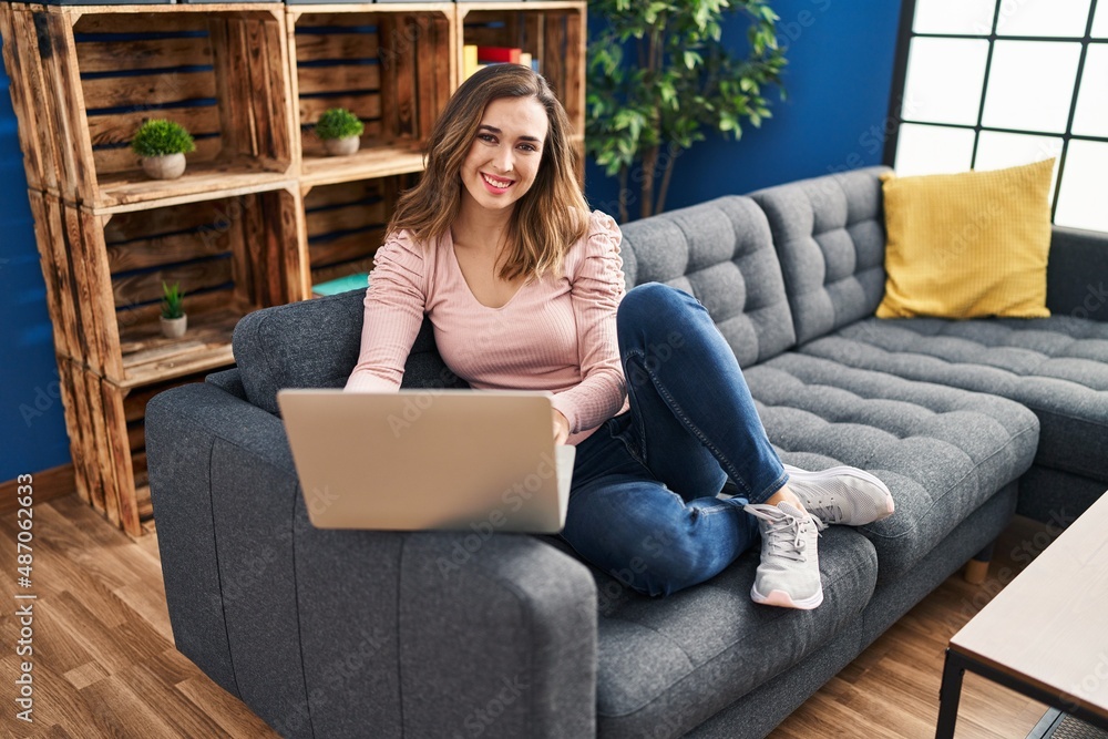 Young woman using laptop sitting on sofa at home Young woman using laptop sitting on sofa at home