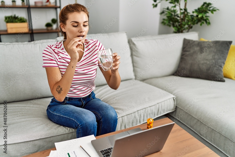 Young woman taking pills working and sitting on sofa at home