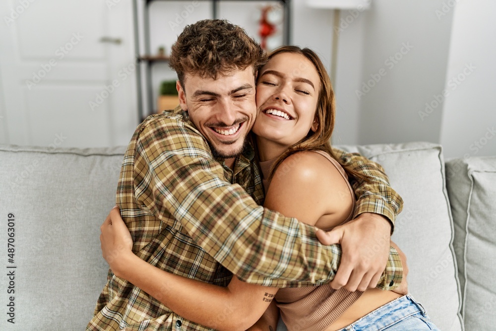 Young hispanic couple smiling happy and hugging sitting on the sofa at home.