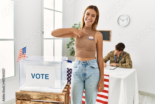 Young american voter woman smiling happy pointing with finger to baddge at electoral college. photo