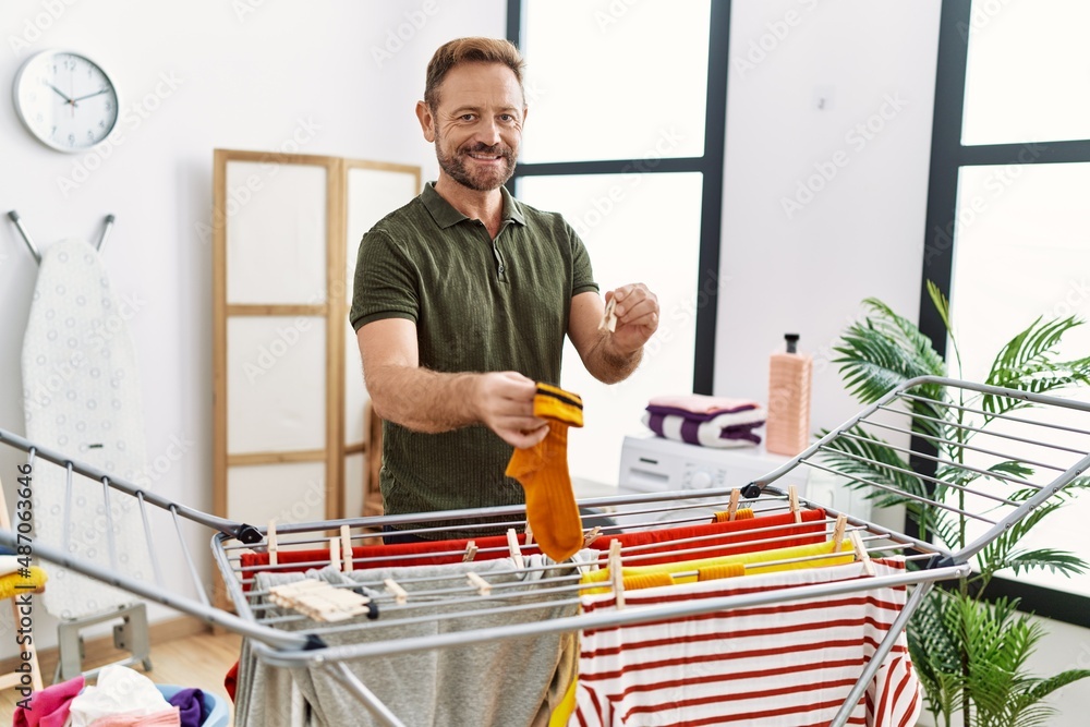 Middle age hispanic man hanging clothes at clothesline at laundry room