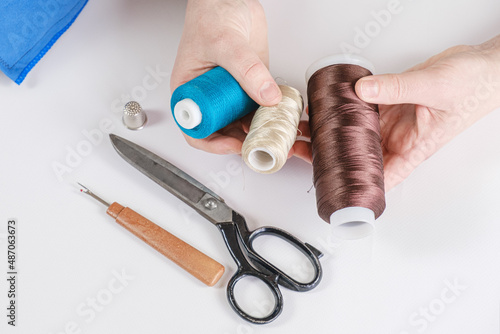 Woman holds spools of thread of different colors in her hands. There are scissors and a seam ripper on the table. Seamstress workplace, tools for sewing and repair clothes.