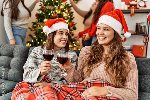 Group of young hispanic women on christmas meeting. Two woman sitting on the sofa toasting with wine at home.