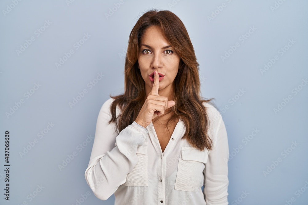 Hispanic woman standing over isolated background asking to be quiet with finger on lips. silence and secret concept. Hispanic woman standing over isolated background asking to be quiet with finger on lips. silence and secret concept.
