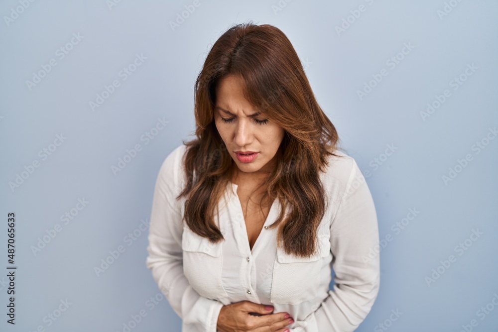 Hispanic woman standing over isolated background with hand on stomach because indigestion, painful illness feeling unwell. ache concept. Hispanic woman standing over isolated background with hand on stomach because indigestion, painful illness feeling unwell. ache concept.