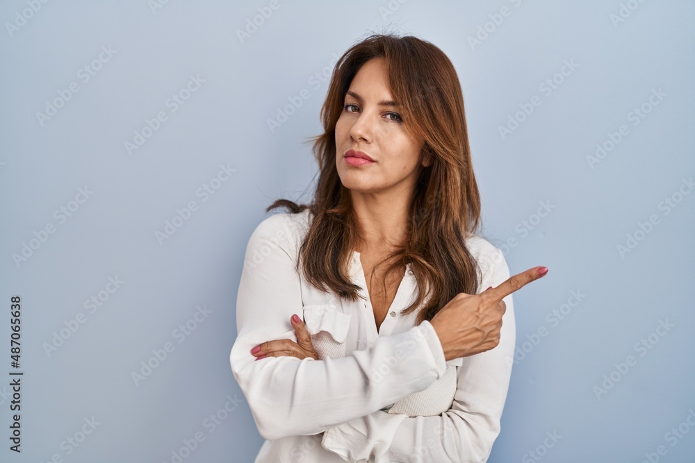 Hispanic woman standing over isolated background pointing with hand finger to the side showing advertisement, serious and calm face Hispanic woman standing over isolated background pointing with hand finger to the side showing advertisement, serious and calm face