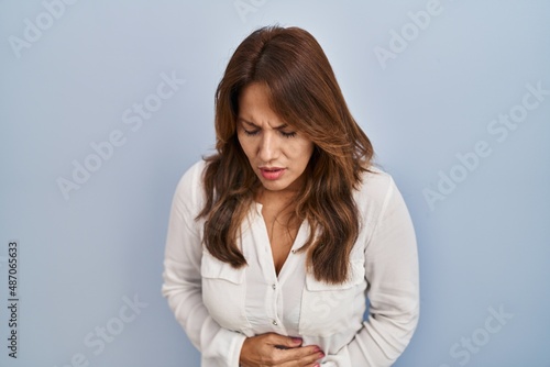 Hispanic woman standing over isolated background with hand on stomach because indigestion, painful illness feeling unwell. ache concept.