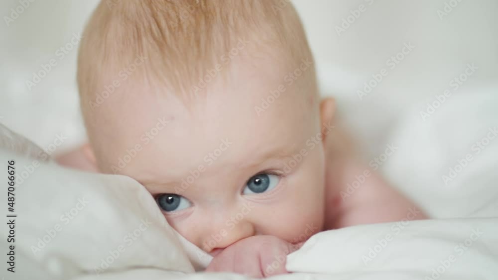 Cute baby lying on bed. Adorable infant with gray eyes sucking blanket and yawning while resting on soft bed at home Cute baby lying on bed. Adorable infant with gray eyes sucking blanket and yawning while resting on soft bed at home