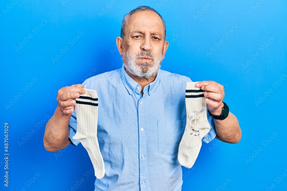 Handsome senior man with beard holding clean andy dirty socks puffing cheeks with funny face. mouth inflated with air, catching air. Handsome senior man with beard holding clean andy dirty socks puffing cheeks with funny face. mouth inflated with air, catching air.