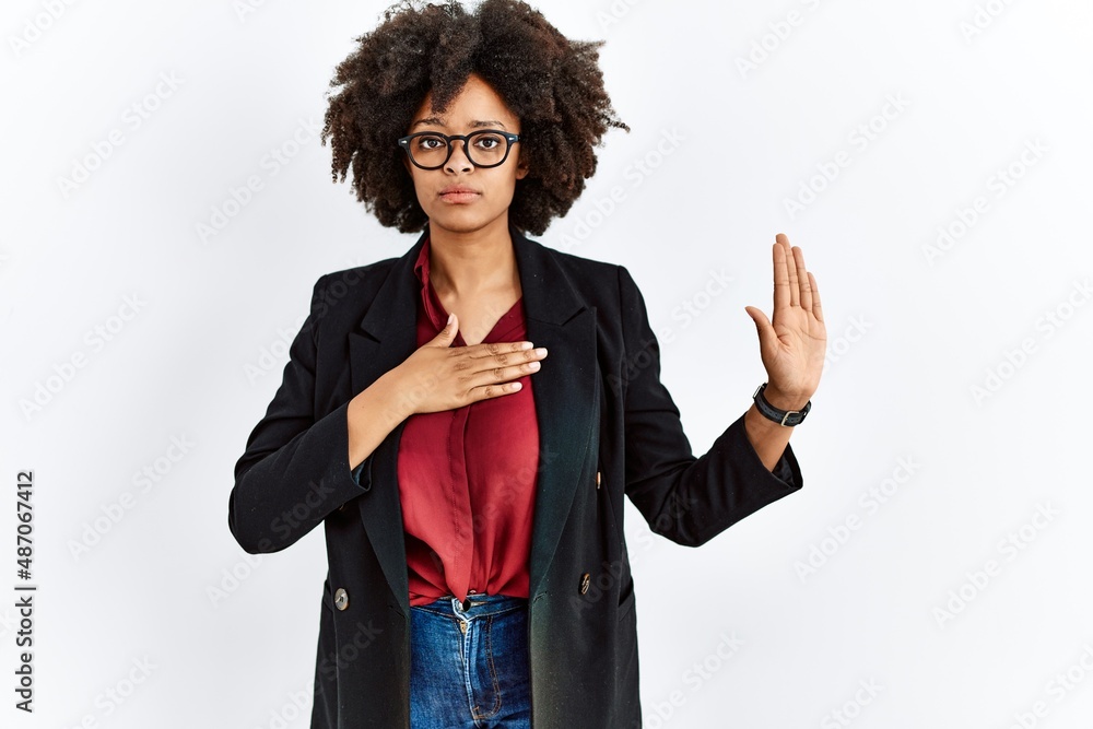 African american woman with afro hair wearing business jacket and glasses swearing with hand on chest and open palm, making a loyalty promise oath African american woman with afro hair wearing business jacket and glasses swearing with hand on chest and open palm, making a loyalty promise oath