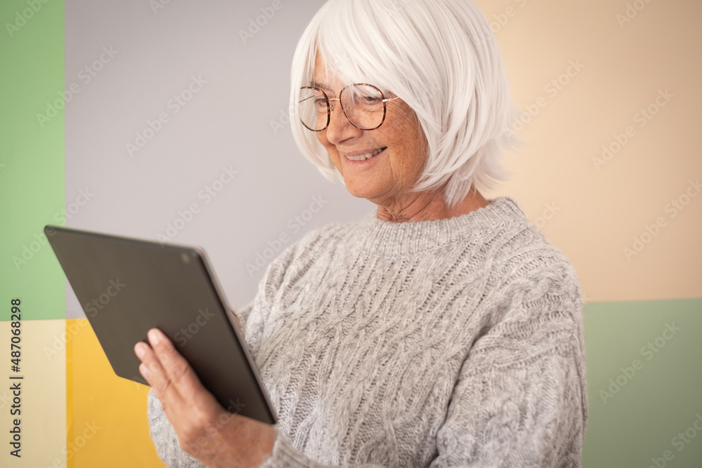 Smiling caucasian senior woman holding using digital tablet, isolated on colorful background, copy space for text, logo, advertising. Mature elderly female enjoy tech and social