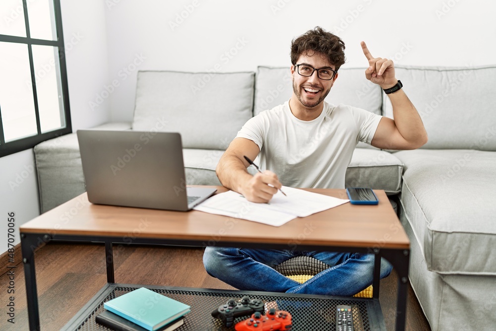 Hispanic man doing papers at home smiling amazed and surprised and pointing up with fingers and raised arms. Hispanic man doing papers at home smiling amazed and surprised and pointing up with fingers and raised arms.