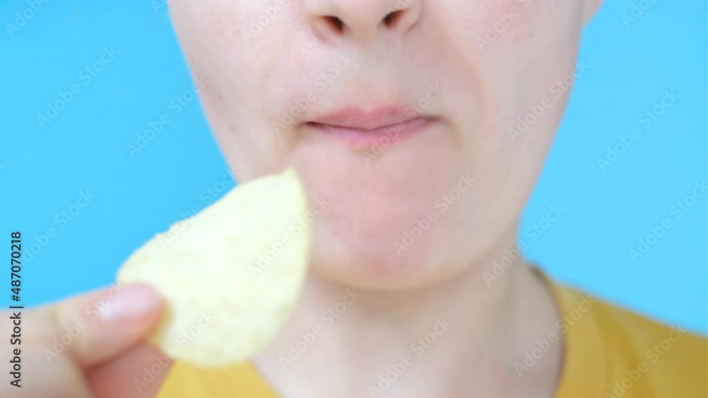A young woman holding potato crisps on blue background close-up. A young woman holding potato crisps on blue background close-up.