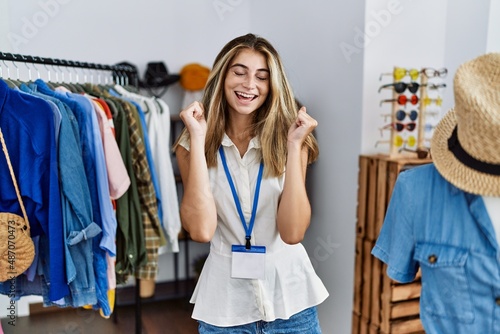 Young blonde woman working as manager at retail boutique excited for success with arms raised and eyes closed celebrating victory smiling. winner concept.
