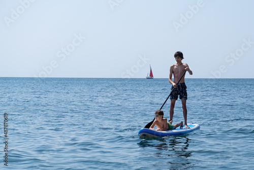 A young sports man with a child sails on a sup in the sea. Healthy lifestyle concept © Irina