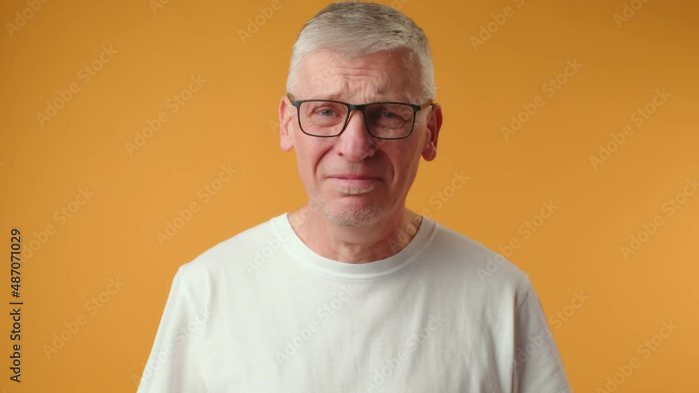 Sad senior man starting to cry over yellow background Sad senior man starting to cry over yellow background