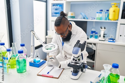 Young african american man wearing scientist uniform using loupe at laboratory