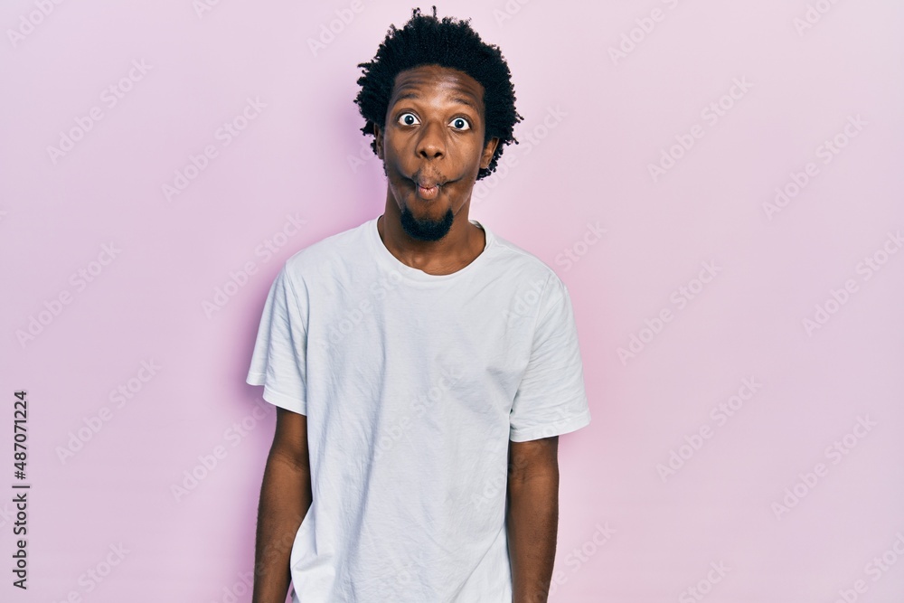Young african american man wearing casual white t shirt making fish face with lips, crazy and comical gesture. funny expression. Young african american man wearing casual white t shirt making fish face with lips, crazy and comical gesture. funny expression.