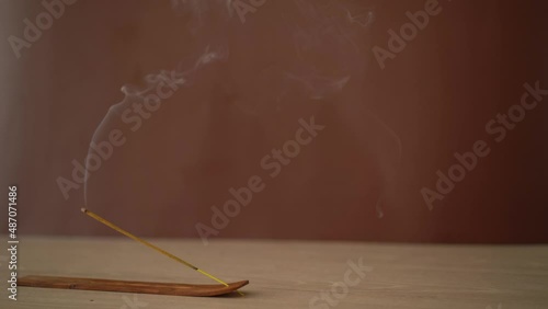 Smoldering incense on stand against brown background.
