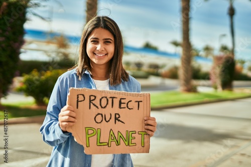 Young latin girl smiling happy holding protect our planet banner at the city. © Krakenimages.com