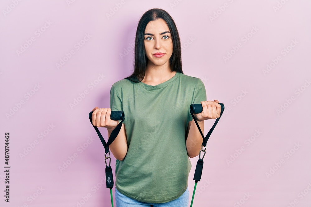 Beautiful woman with blue eyes training arm resistance with elastic arm bands relaxed with serious expression on face. simple and natural looking at the camera. Beautiful woman with blue eyes training arm resistance with elastic arm bands relaxed with serious expression on face. simple and natural looking at the camera.