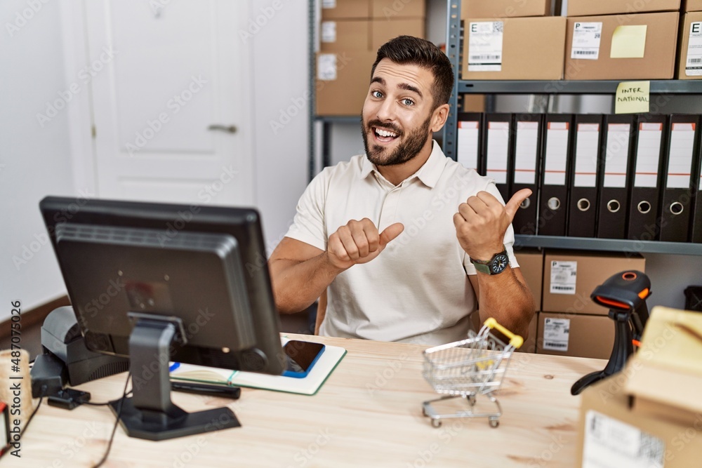 Handsome hispanic man working at small business commerce pointing to the back behind with hand and thumbs up, smiling confident Handsome hispanic man working at small business commerce pointing to the back behind with hand and thumbs up, smiling confident