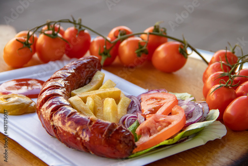 Fast food grilled sausages served at plate together with tomato and lettuce seasonal salad