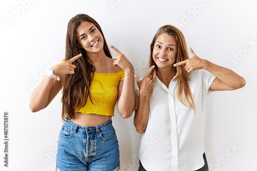 Mother and daughter together standing together over isolated background smiling cheerful showing and pointing with fingers teeth and mouth. dental health concept.