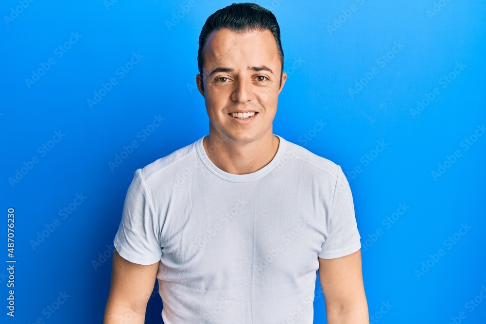 Handsome young man wearing casual white t shirt with a happy and cool smile on face. lucky person. Handsome young man wearing casual white t shirt with a happy and cool smile on face. lucky person.