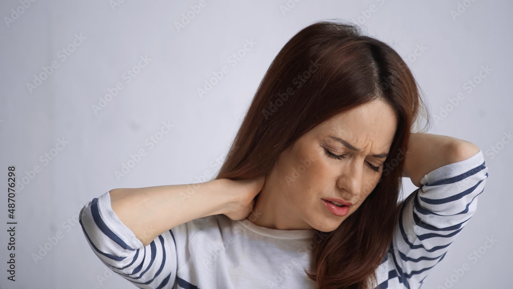 unhappy woman touching painful neck and frowning with closed eyes on grey background unhappy woman touching painful neck and frowning with closed eyes on grey background