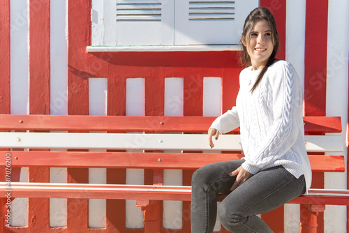 Young girl sitting on a bench with a wall of red and white lines in the background.