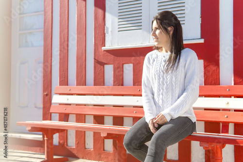 Young girl sitting on a bench with a wall of red and white lines in the background.
