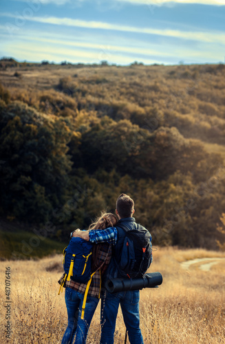 Rear view of couple with backpacks hiking together in nature on autumn day.