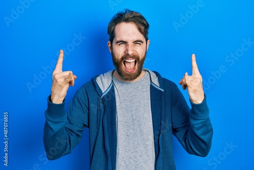 Caucasian man with beard wearing casual sweatshirt shouting with crazy expression doing rock symbol with hands up. music star. heavy concept.