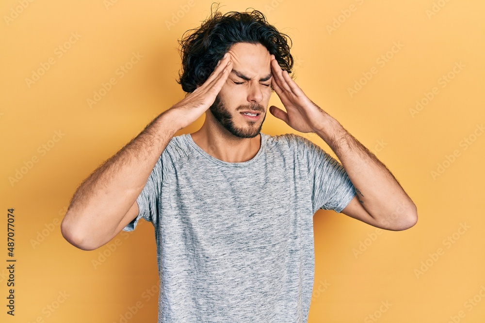 Handsome hispanic man wearing casual grey t shirt with hand on head, headache because stress. suffering migraine. Handsome hispanic man wearing casual grey t shirt with hand on head, headache because stress. suffering migraine.