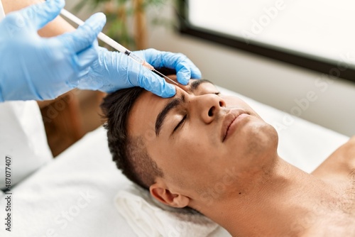 Young hispanic man relaxed having antiaging treatment at beauty center