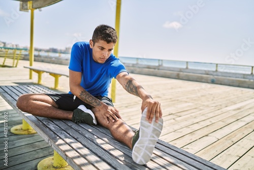 Young hispanic man stretching leg muscles outdoors