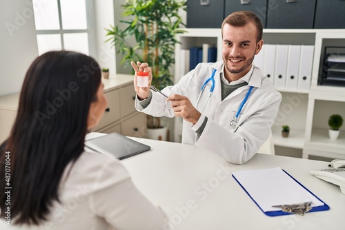 Man and woman doctor and patient having medical consultation holding urine analysis bottle at clinic