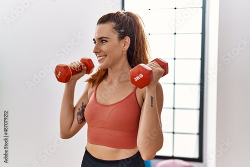 Young redhead woman smiling confident training with dumbbells at sport center